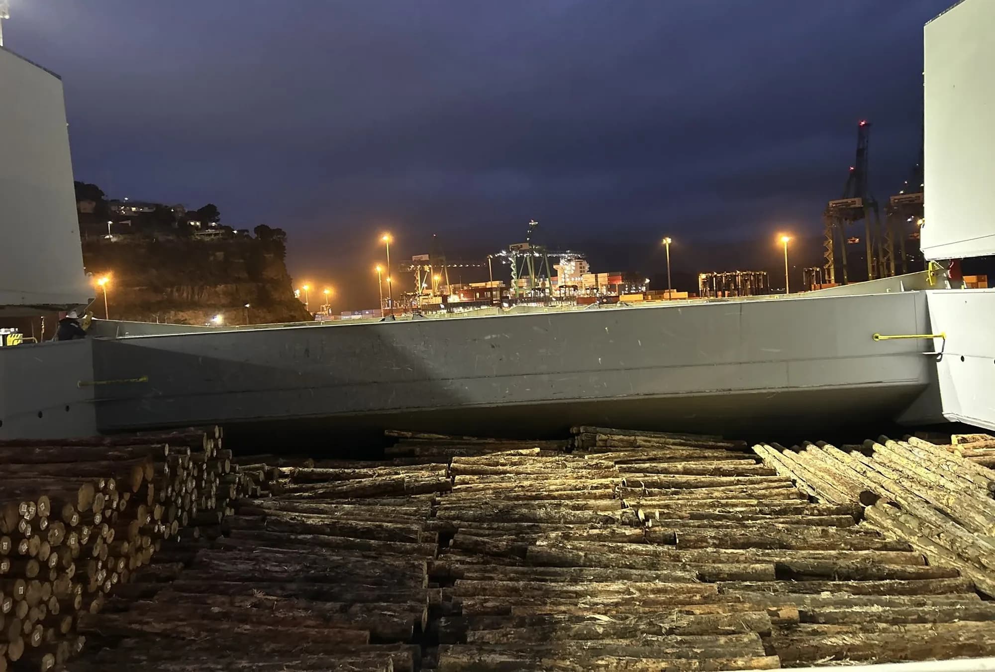 Logs stacked on the wharf alongside a loading vessel at night